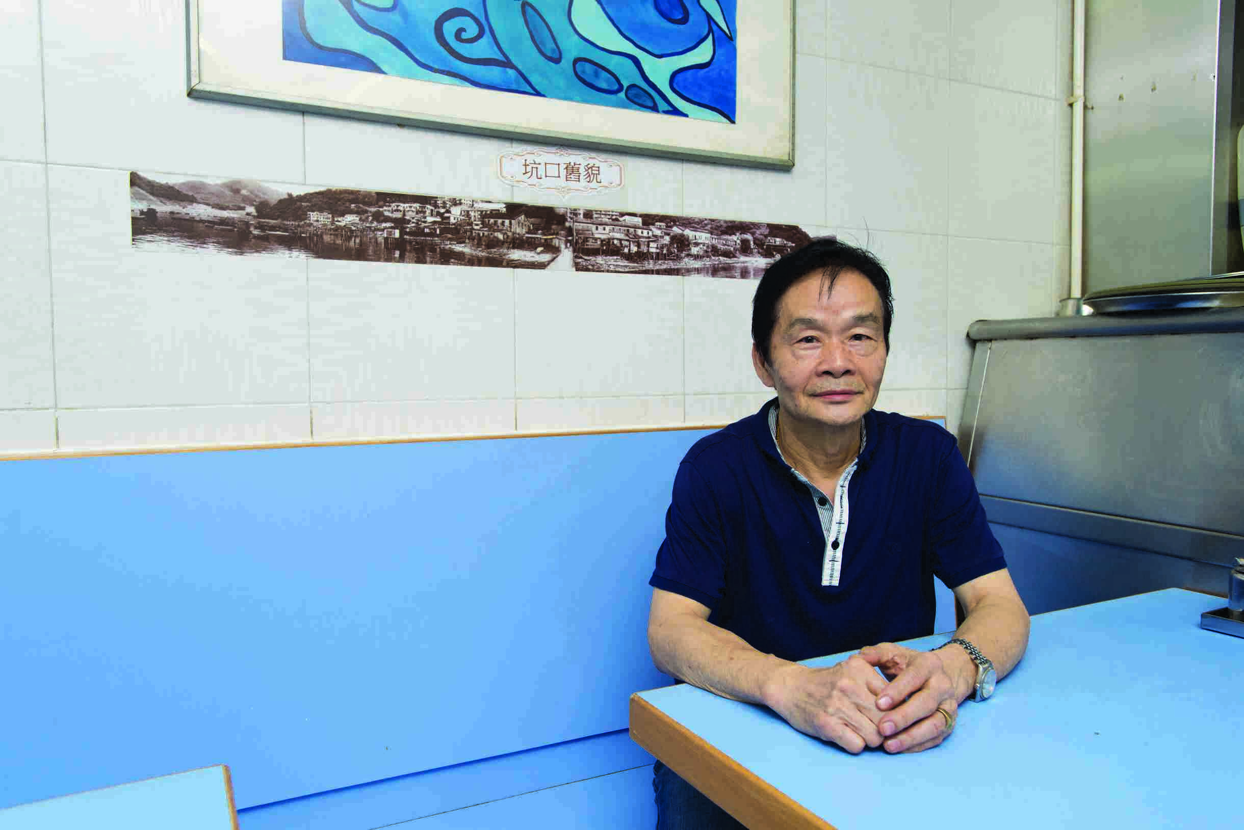 張錫金背後一幀全景相，展示昔日坑口村民傍海而居，該處現已填成馬路及大廈。