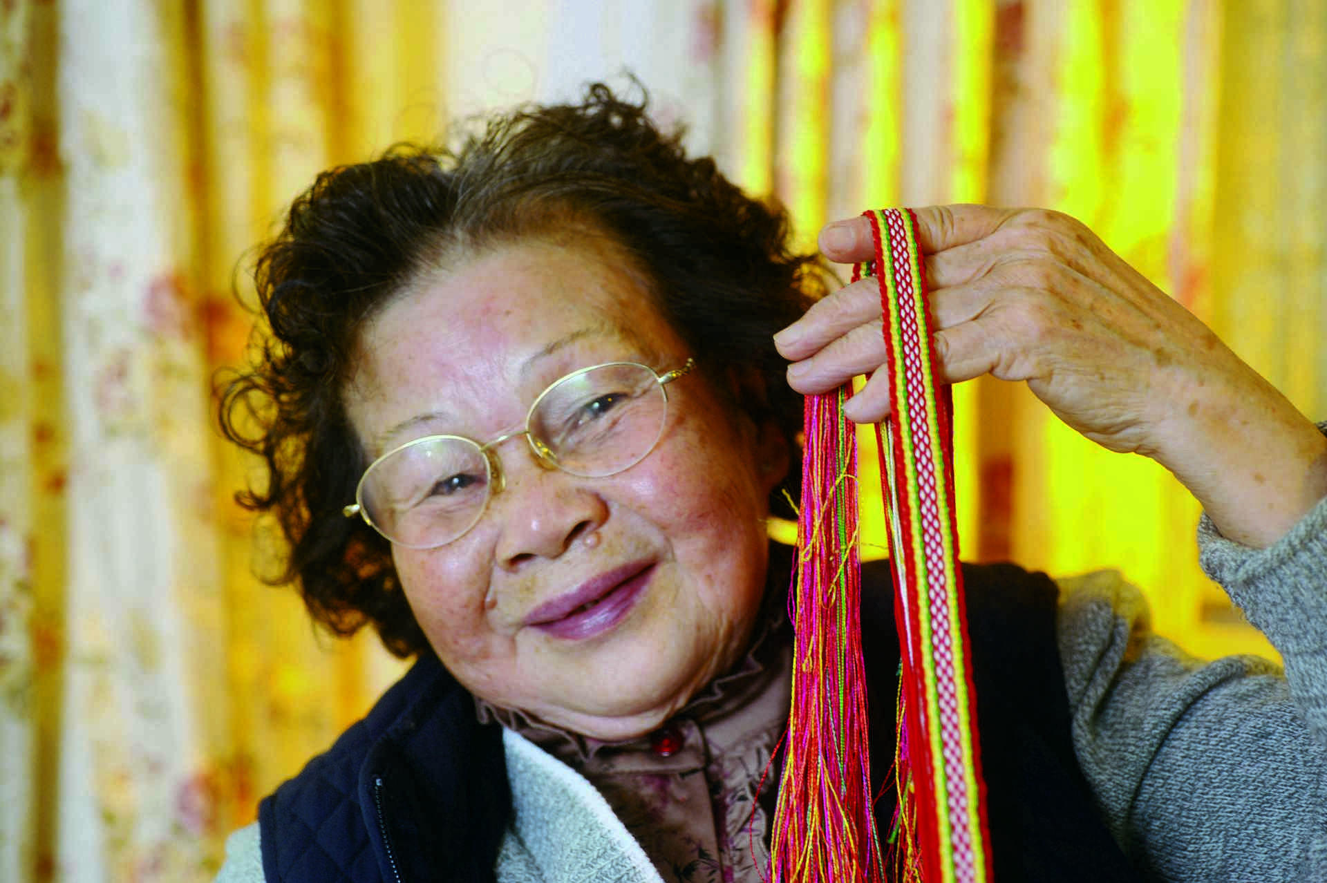 蔡清妹手執麻子花花帶，細說從前如何為包頭巾作綴飾，為涼帽、圍裙配上漂亮繫帶。
